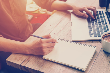 Young business man hand writing and using laptop in coffee shop with vintage filter.の写真素材