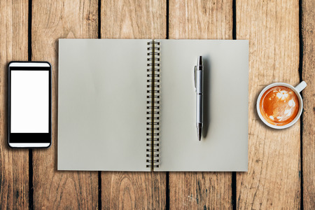 smartphone coffee cup and notebook on wooden background with space.の写真素材