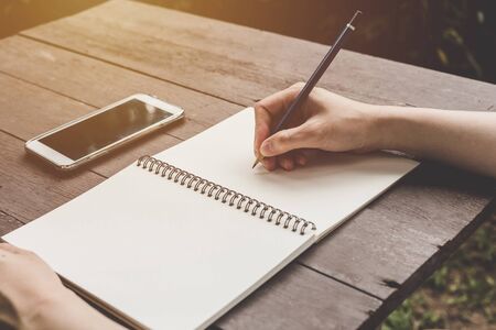 close up hand woman writing notebook on wood table background.の写真素材