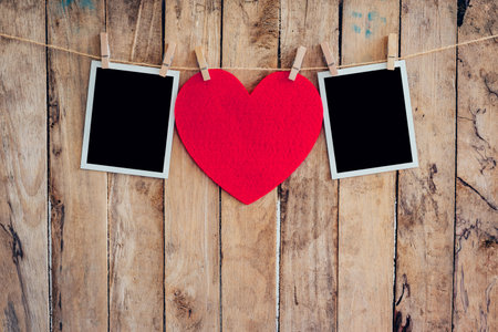 Red heart and two photo frame hanging on clothesline rope with wooden background.の写真素材
