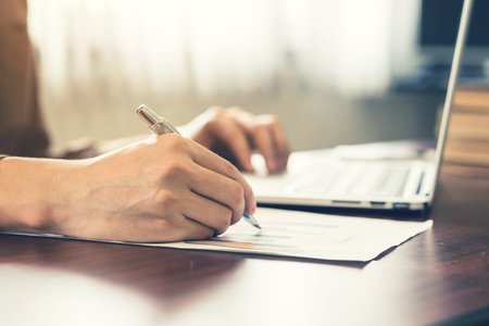 Close up hand business man writing book and using laptop in the office with sunlight. Vintage toned...