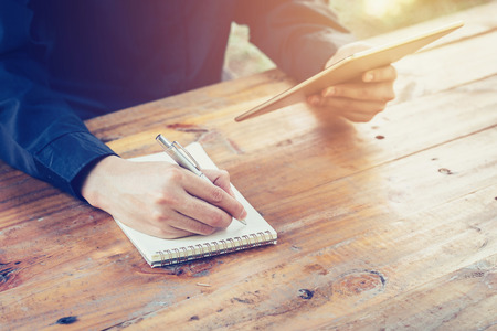 young business man writing note pad and using tablet in coffee shop witn vintage filter.の写真素材
