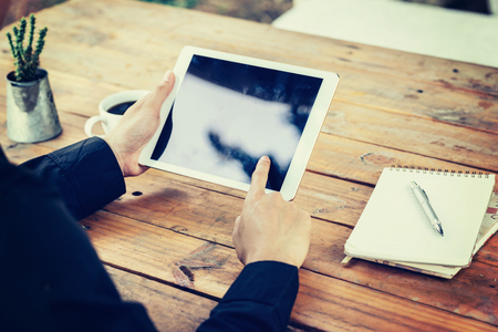 Business man hand holding and using tablet on table in coffee shop with vintage toned filter.の写真素材
