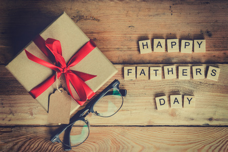 Happy father's day block and gift box with glasses on wood background.の写真素材