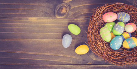 Colorful easter egg and nest on wooden background with space.