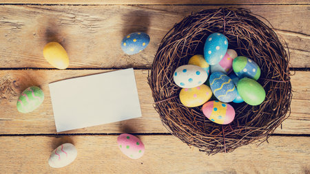 Colorful easter egg in nest and paper card on wood background with space.