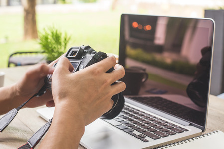 Man hands hand holding camera and using laptop computer in coffee shop.の写真素材