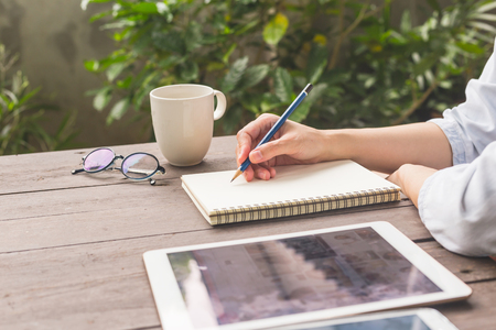 Hand woman writing notebook on wood table with cup coffe and tablet.の写真素材