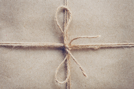 String or twine tied in a bow on brown kraft paper texture.の写真素材