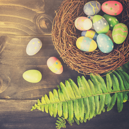 Colorful easter eggs in neat and green leave on table wooden background with space.の写真素材