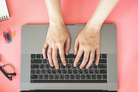 Women typing on laptop in pink pastel colourful office with accessoriesの写真素材
