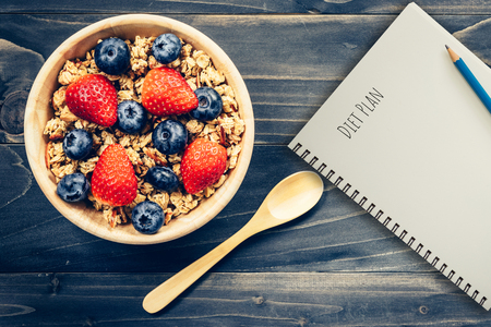 Homemade granola and fresh berries on wood table with note book and text diet plan concept, copy space.の写真素材