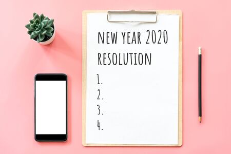2020 New year concept. Resolution list in stationery, blank clipboard, smartphone, pot plant on pink pastel color with copy spaceの写真素材