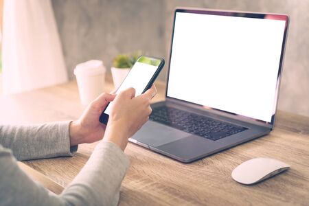 Hipster women holding phone and using laptop on wooden table in coffee shop.の写真素材
