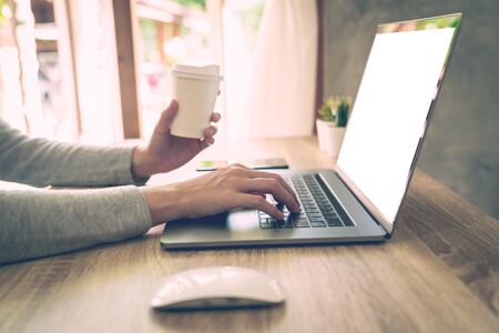 Woman holding coffee and using laptop on wooden table in officeの写真素材