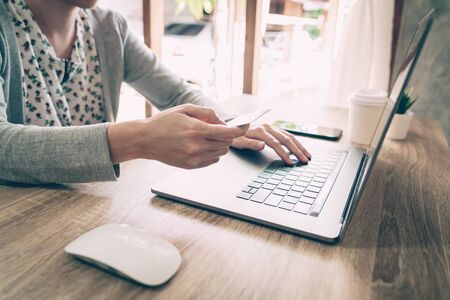 Asian woman holding credit card paying for shopping in computer laptop on wooden tableの写真素材