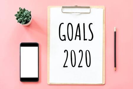 New year concept. Goals 2020 and stationery, blank clipboard, smartphone, pot plant on pink pastel color with copy spaceの写真素材