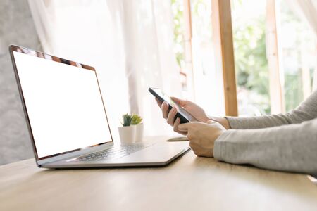 Asian woman holding phone and using computer laptop on wooden tableの写真素材