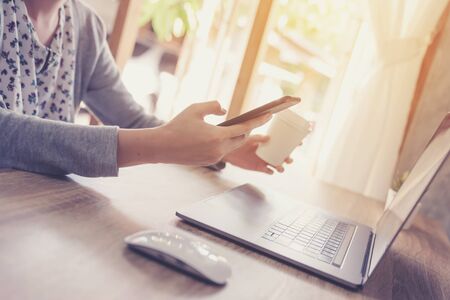 Woman holding coffee and using laptop on wooden table in officeの写真素材