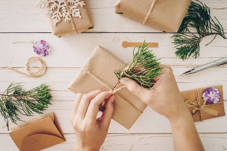 Close up of hands holding wrapping gift box on wooden table with xmas decoration.の写真素材