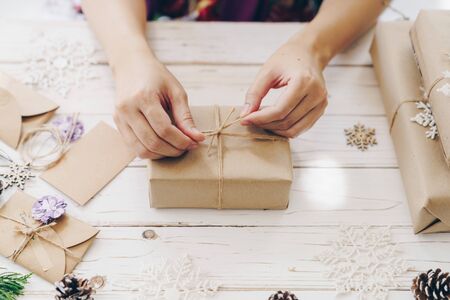 Close up of hands holding wrapping gift box on wooden table with xmas decoration.の写真素材