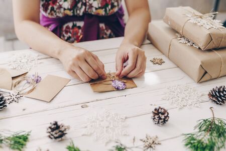 Close up of hands holding wrapping gift box and christmas card on wooden table with xmas decoration.の写真素材