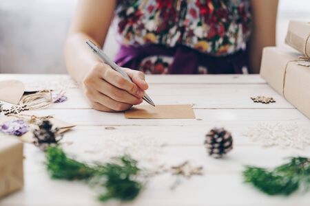 Close up of hands woman writing empty wishlist and christmas card on wooden table with xmas decoration.の写真素材