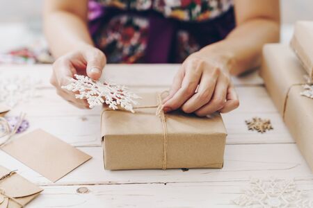 Close up of hands holding wrapping gift box on wooden table with xmas decoration.の写真素材