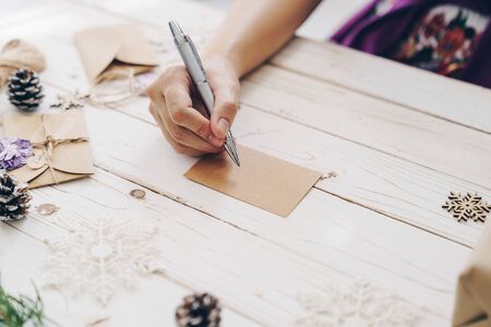 Close up of hands woman writing empty wishlist and christmas card on wooden table with xmas decoration.の写真素材