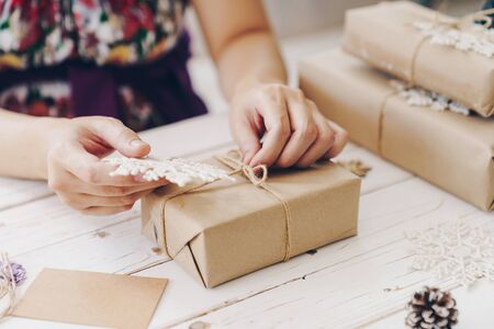 Close up of hands holding wrapping gift box on wooden table with xmas decoration.の写真素材