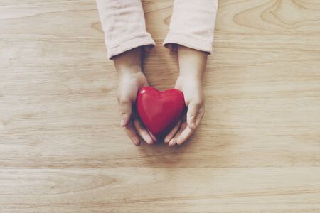 girl hand holding heart on wood table backgroundの写真素材
