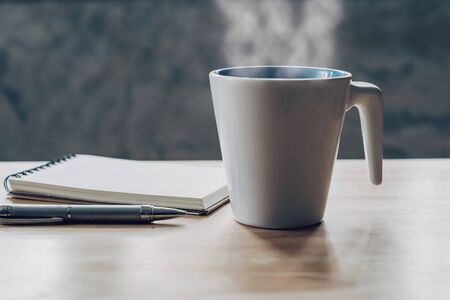 cup of coffee and notepad with pen on wood tableの写真素材