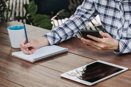 woman hand writing notepad and holding phone on wooden table at coffee shopの写真素材