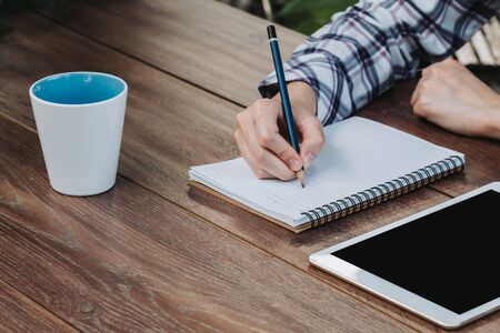 woman hand writing notepad and holding phone on wooden table at coffee shopの写真素材