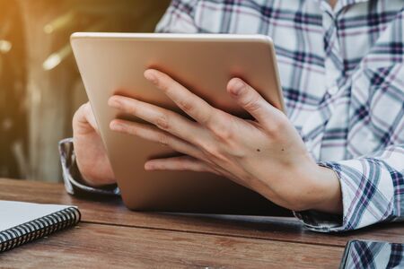 Woman hand holding tablet on wooden table at work from home.の写真素材