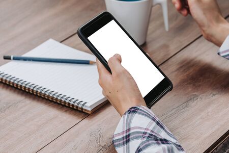 Woman hand holding phone on wooden table at work from homeの写真素材