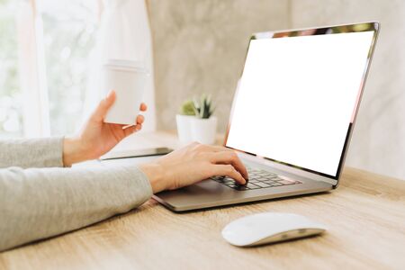 woman using laptop and holding coffee working on wooden tableの写真素材
