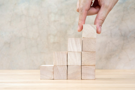 Hand arranging wood block stacking as step stair on wooden table. Business concept for growth...