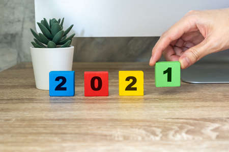 2021 happy new year, hand holding wood block on wood table desktop computer and pot plant. new year conceptの写真素材
