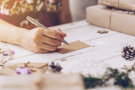 Woman hand writing beautiful Christmas card at tableの写真素材