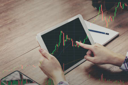 Trader holding in hands tablet researching stock market to proceed right investment solutions.の写真素材
