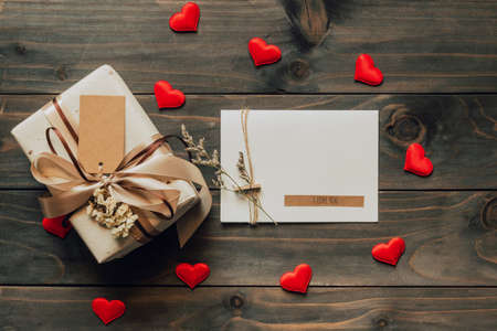 Gift box and greeting card with bow ribbon and paper hearts on wooden table for Valentines day. copy space.の写真素材