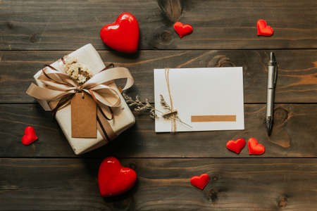 Gift box and greeting card with bow ribbon and paper hearts on wooden table for Valentines day. copy space.の写真素材
