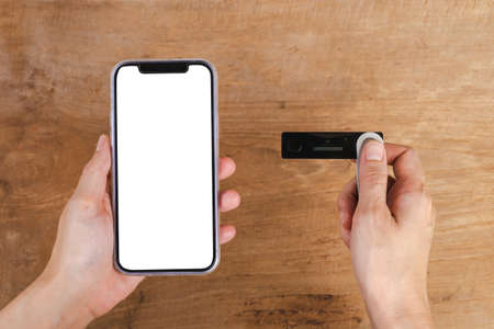 Hand holding mobile phone and hardware wallet on wooden tableの写真素材