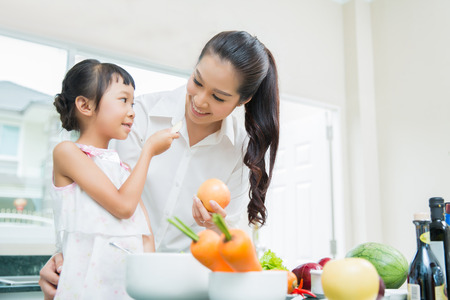 The daughter is feeding her mother eating fruit. While cooking in the kitchenの写真素材