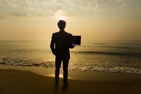 Business Man Standing on the beach in the morning. Are using a notebook computer.

の写真素材