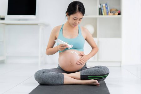 Pregnant woman, she is applying cream on the stomach, preventing skin cracks.の写真素材
