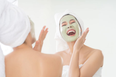 Asian woman is applying facial mask. She is looking in the mirror.の写真素材