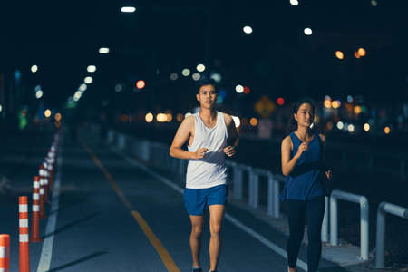 Asian couple jogging in the city streets at nightの写真素材