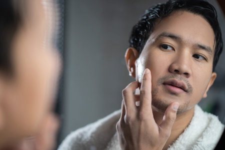 Asian man looking in the mirror at bathroom He touch his face